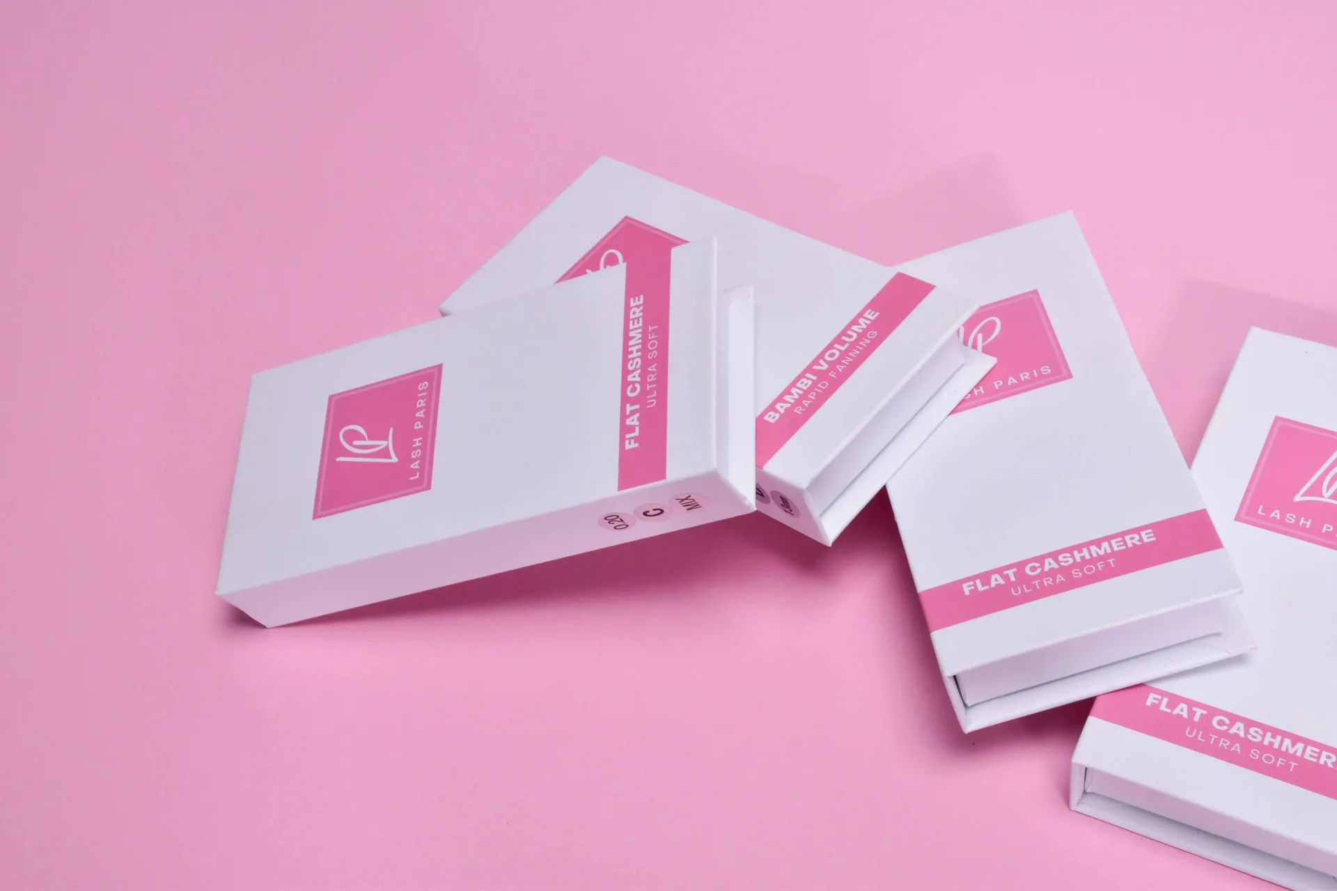 Lash Paris flat cashmere and bambi volume lash boxes scattered on a pink background
