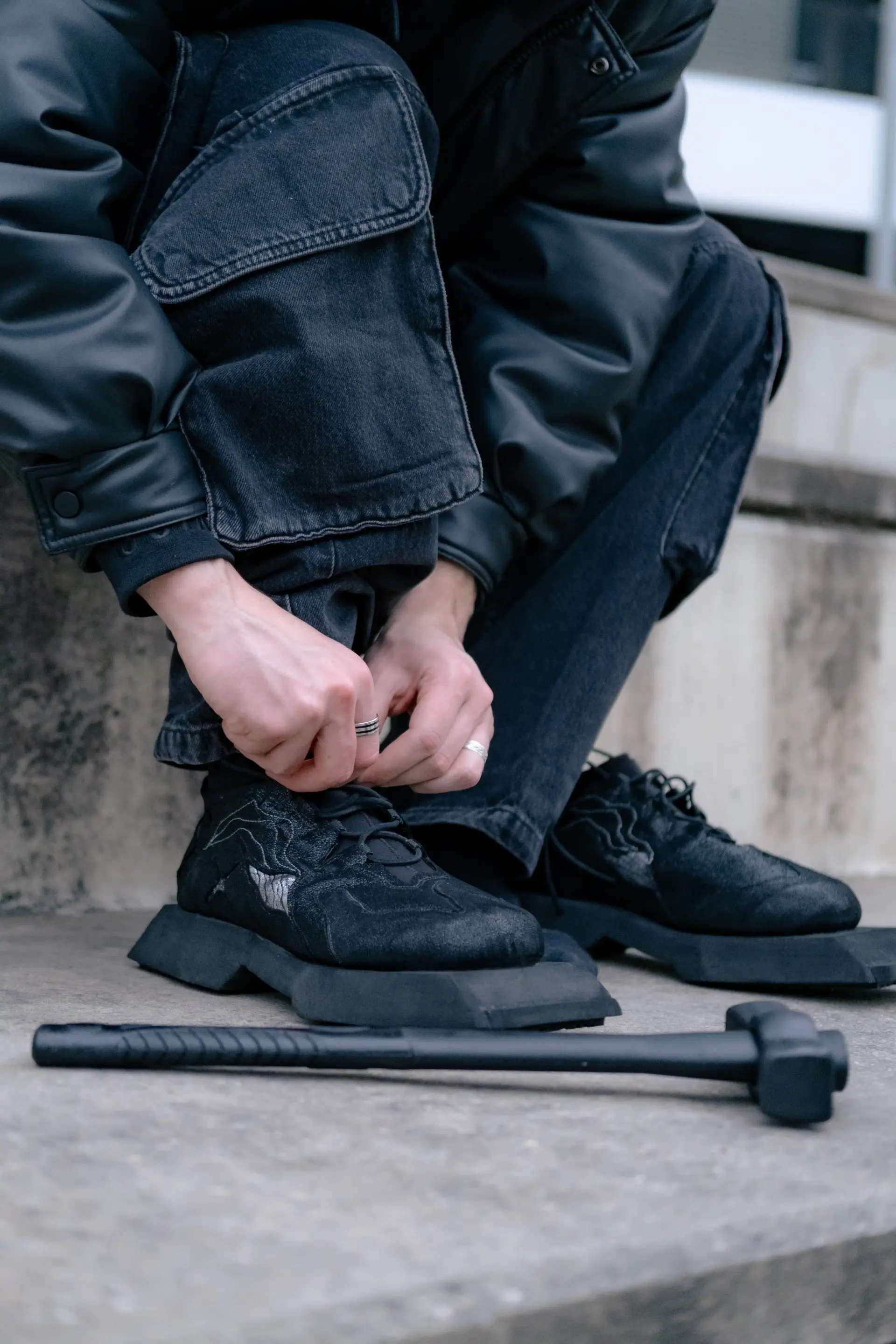 Model crouching to lace the black sneakers, mallet resting on the concrete