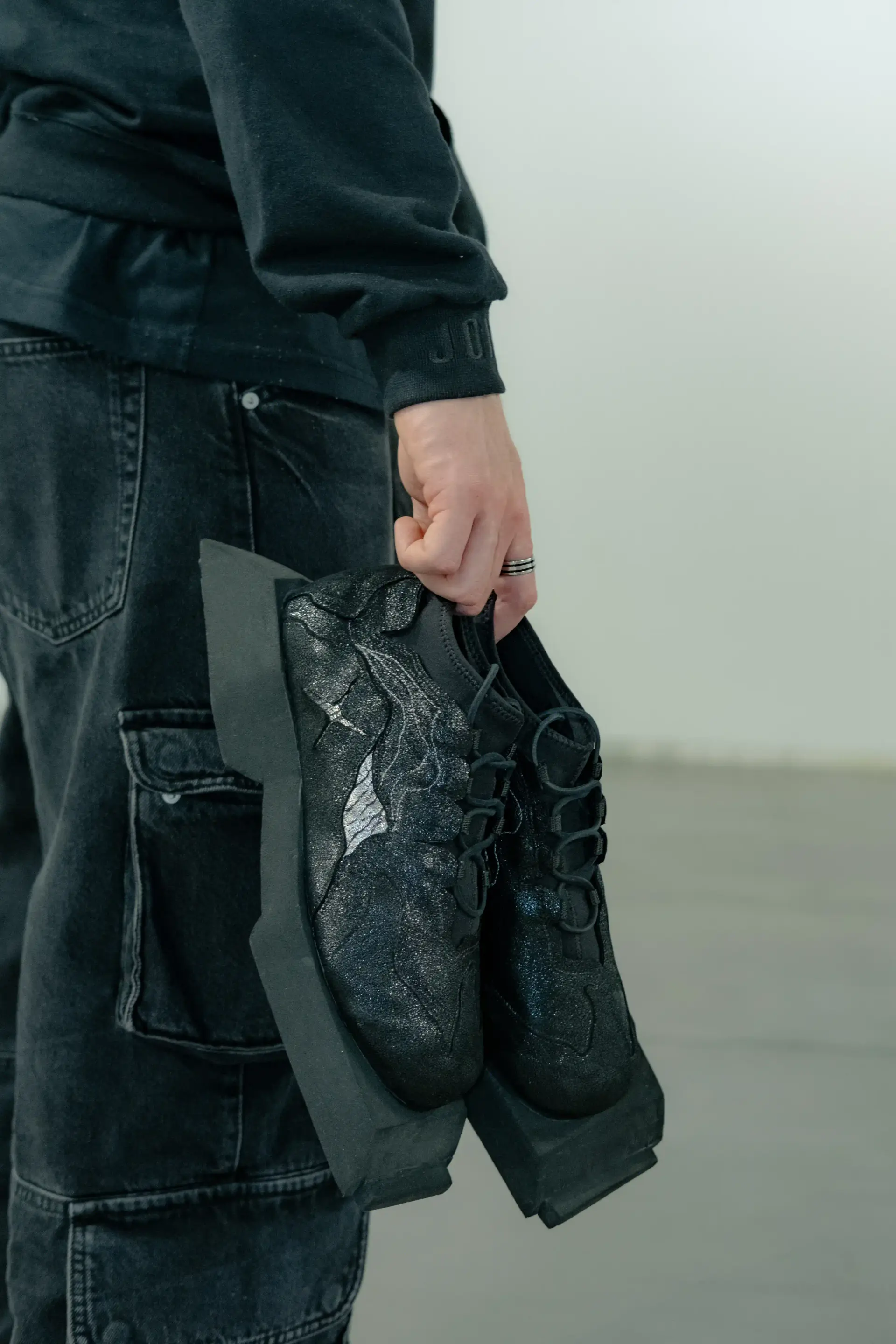 Model carrying the pair of black sneakers in one hand at their side
