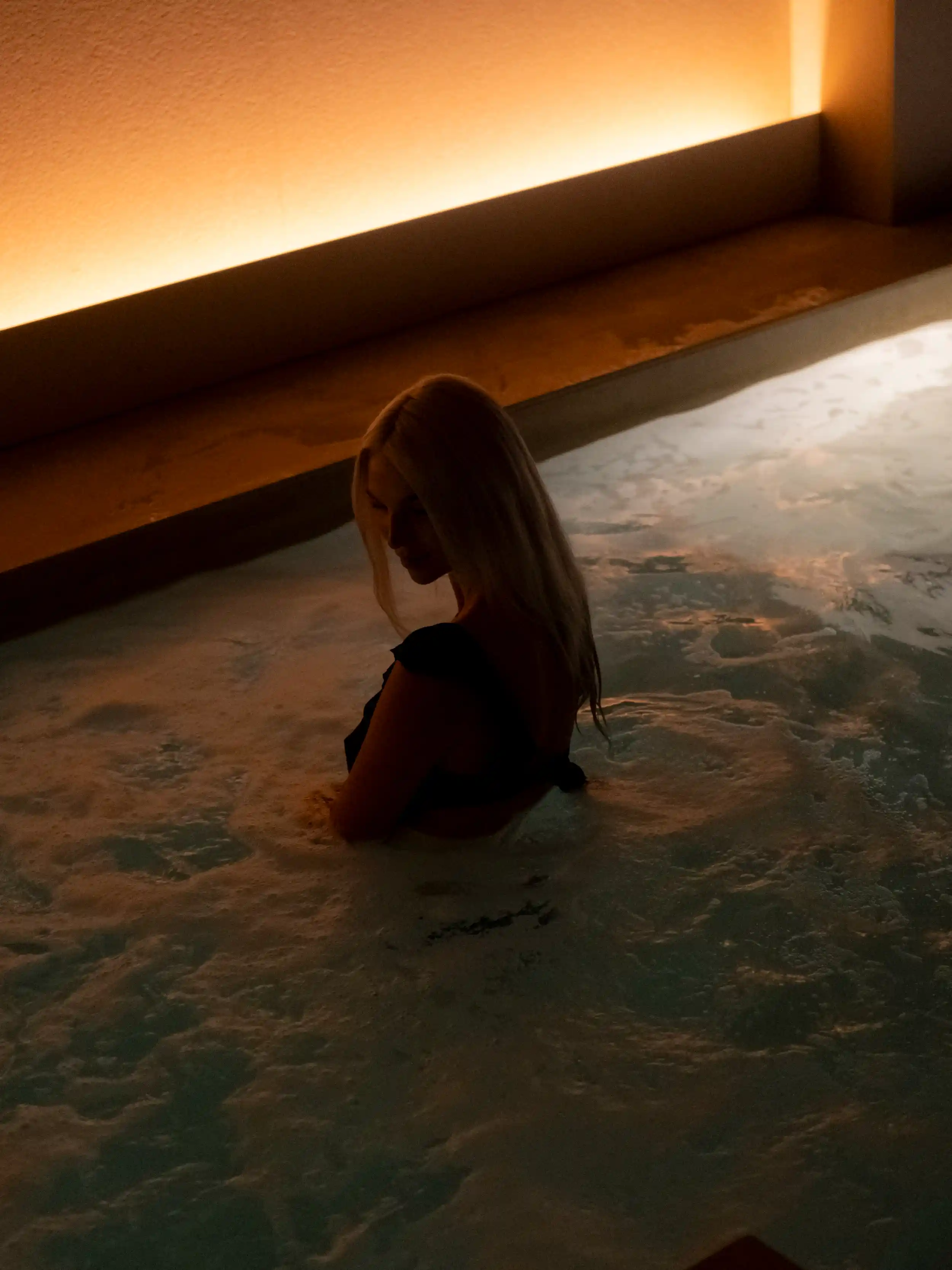 Model waist-deep in a bubbling whirlpool, backlit by warm amber cove lighting