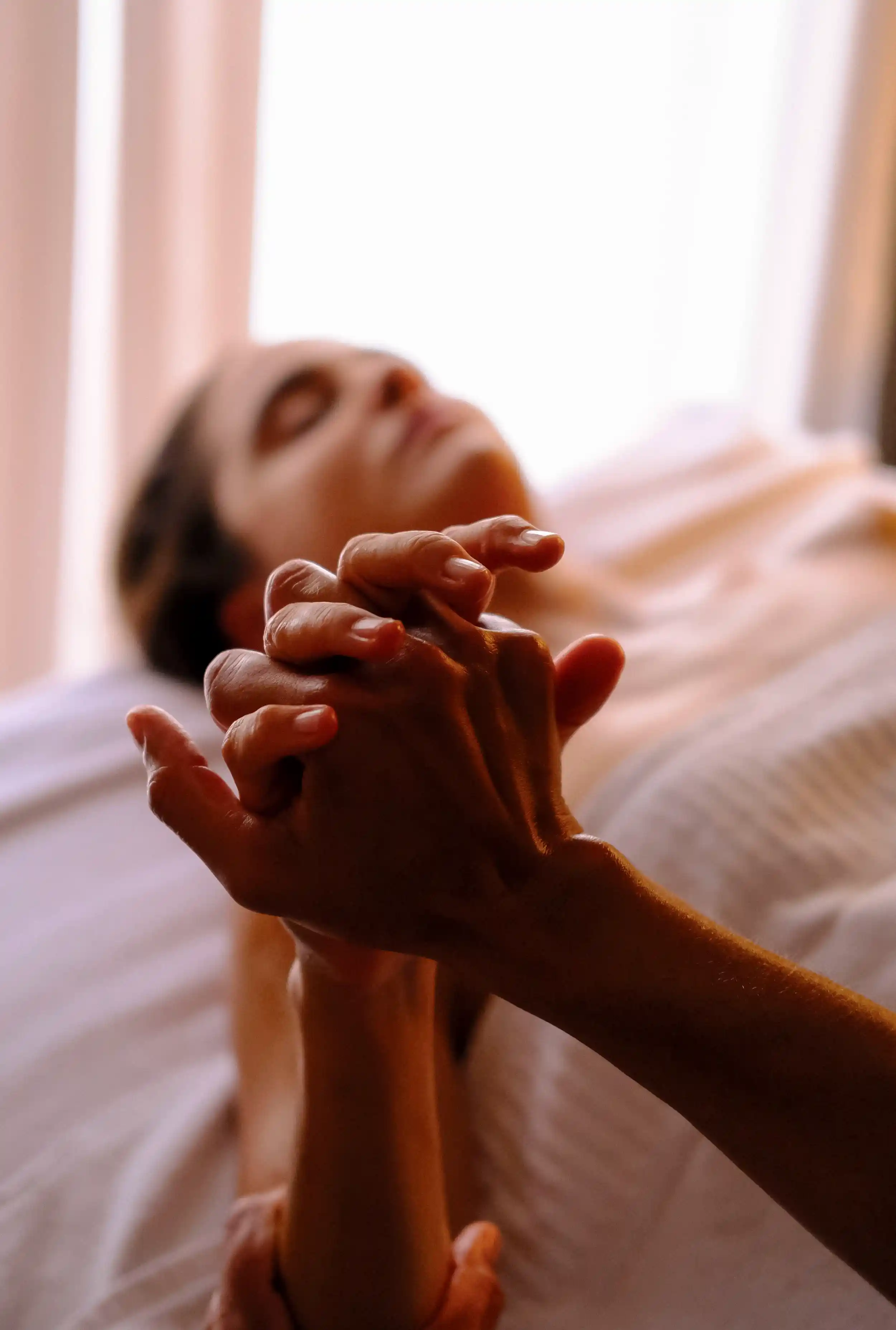 Close-up of a therapist's hands interlaced with a client's hand during a treatment